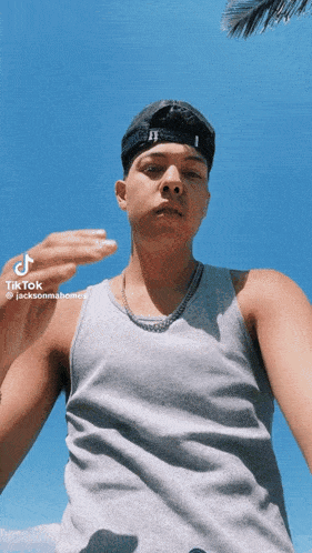 a young man wearing a hat and a tank top is taking a selfie with tik tok