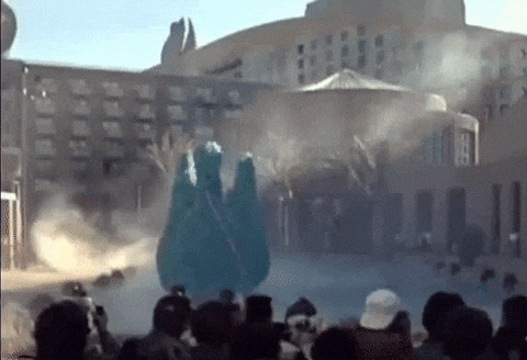 a crowd of people are watching a statue of a dinosaur being displayed in front of a building