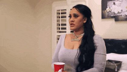 a woman with long black hair is holding a red cup in her hand in a bedroom .