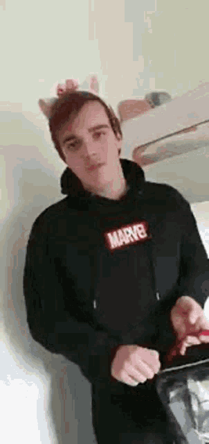a man wearing a hoodie and a headband with cat ears is standing in a kitchen .