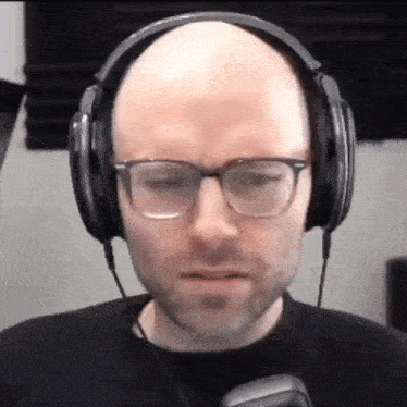 a bald man wearing headphones and glasses is making a funny face .