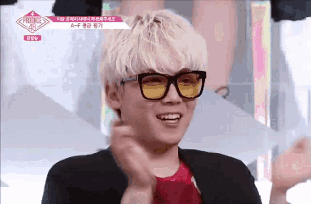 a young man wearing yellow glasses and a red shirt is smiling and clapping