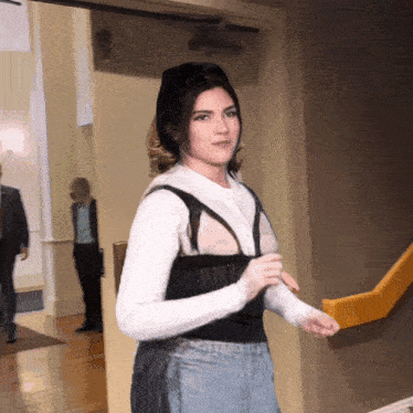 a woman wearing a white shirt and black top is walking down a hallway
