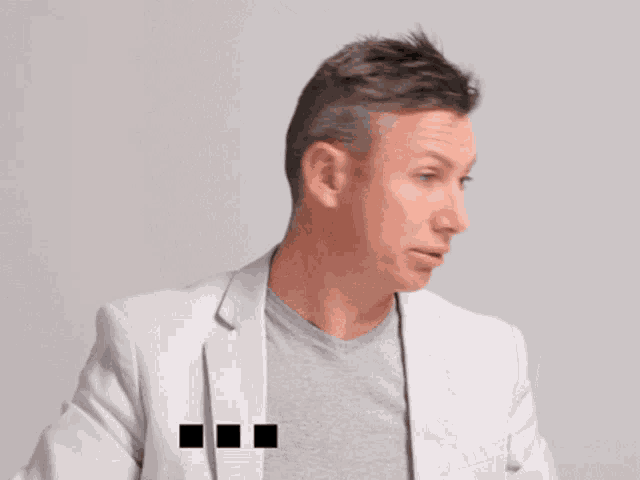 a man wearing a grey shirt and a white jacket has the word okay written on his shirt