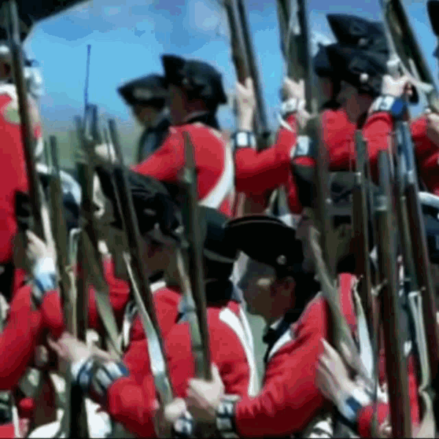 a group of men in red uniforms are holding guns in a line