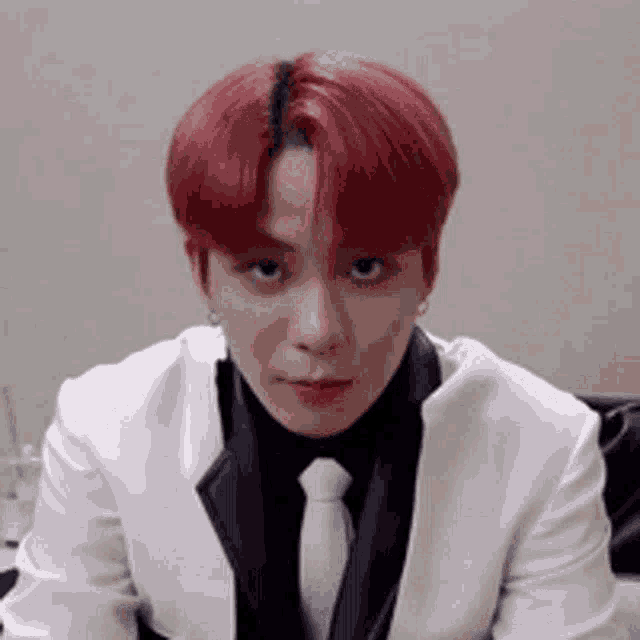 a man with red hair is wearing a white suit and tie and making a funny face .