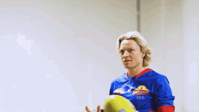 a man wearing a mission shirt holds a yellow soccer ball