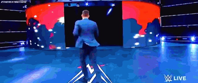 a man in a suit is standing in front of a large screen that says ' wwe live ' on it