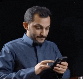 a man in a blue shirt is looking at his cell phone .