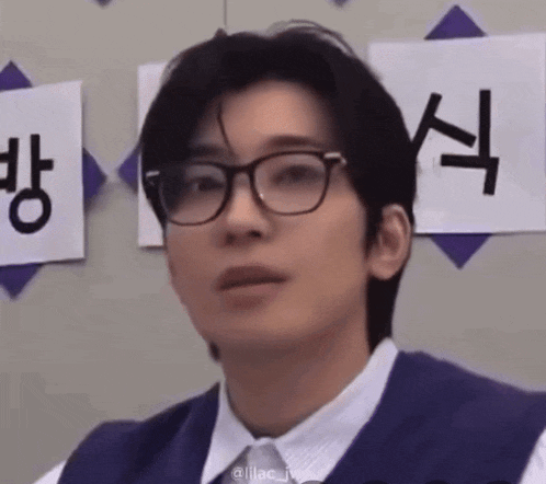 a young man wearing glasses and a vest looks at the camera .