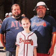 a boy wearing a braves jersey stands with two men
