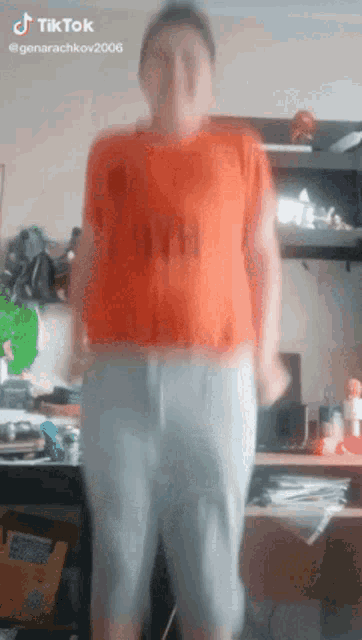 a man in an orange shirt and white pants is dancing in front of a desk with a tiktok watermark on the bottom