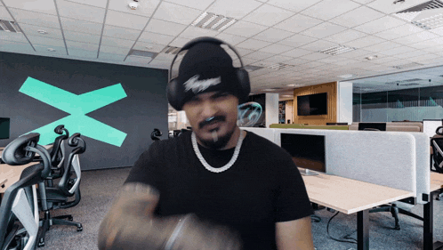 a man wearing headphones and a beanie has a green x on the wall behind him