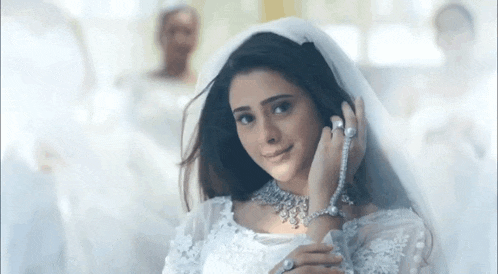a woman in a wedding dress with a veil on her head is smiling .