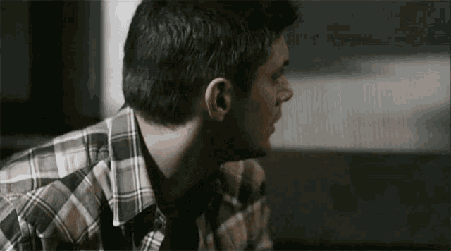 a man in a plaid shirt is sitting on a couch and looking away from the camera .