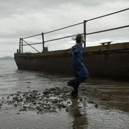 a person in a blue jacket is walking on a muddy beach near a boat