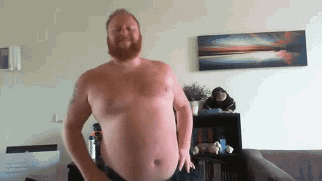 a shirtless man with a beard is standing in front of a painting on the wall