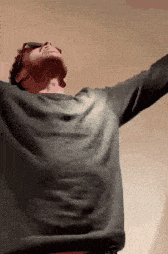 a man with his arms outstretched wearing sunglasses and a grey shirt