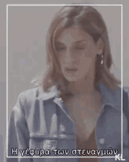 a woman wearing a denim jacket and earrings is standing in front of a white wall .