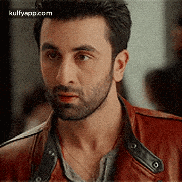 a man with a beard and a red leather jacket is looking at the camera .