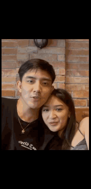 a man and a woman are posing for a picture while sitting in front of a brick wall .