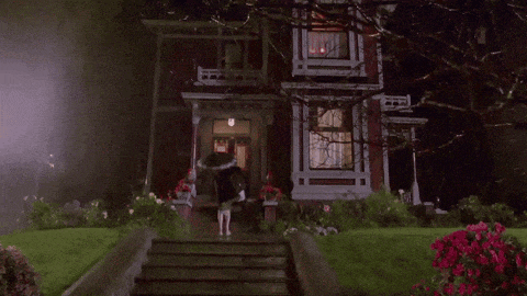 a woman in an umbrella is walking down the stairs of a haunted house at night .
