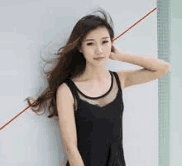 a woman in a black dress is standing next to a white wall .