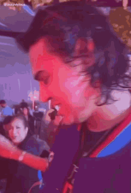 a blurry picture of a man with a purple shirt that says ' auspvicious ' on the bottom right