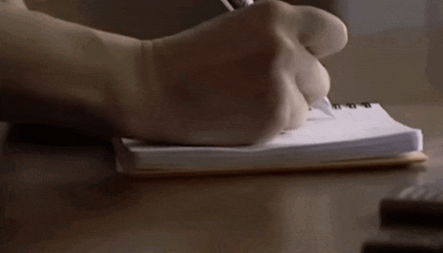 a close up of a person 's hand writing in a notebook
