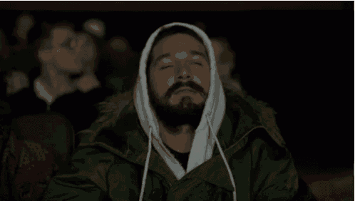 a man with a beard wearing a hooded jacket is watching a movie