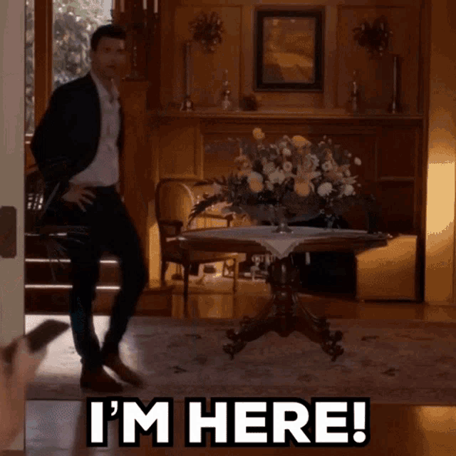 a man in a suit is standing in a living room with the words i 'm here on the floor