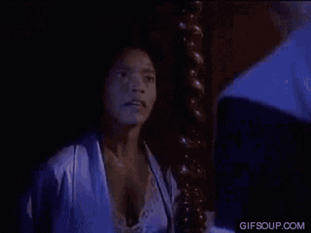 a woman in a blue robe is looking at a man in a blue shirt in a dark room .