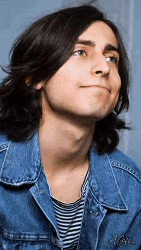 a young man with long hair wearing a denim jacket and striped shirt