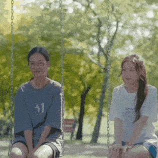 two young women are sitting on swings in a park