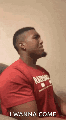 a man in a red shirt is sitting on a couch and making a face .