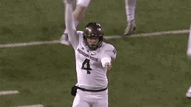 a football player wearing a michigan state jersey is kicking a ball on the field .