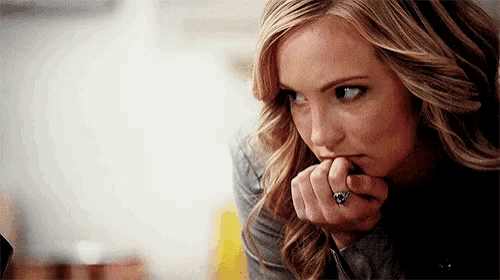 a woman with a ring on her finger is biting her nails and looking at the camera .