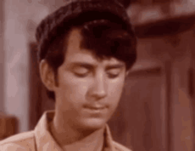 a young man wearing a hat and a shirt is looking down with his eyes closed .
