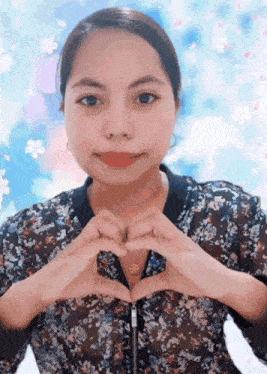 a woman in a floral shirt makes a heart shape with her hands