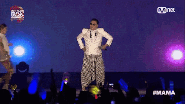 a man in a white jacket and plaid pants stands on a stage at a mnet music awards