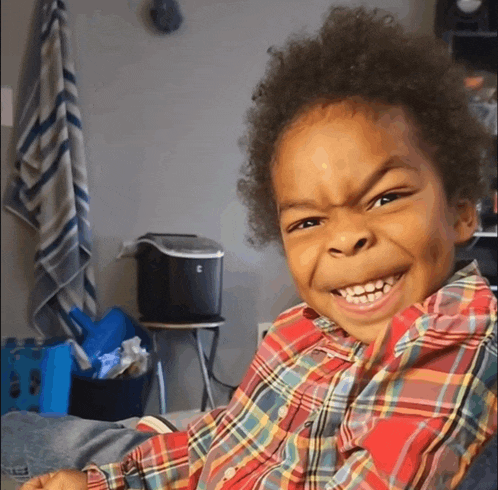 a little boy in a plaid shirt making a face