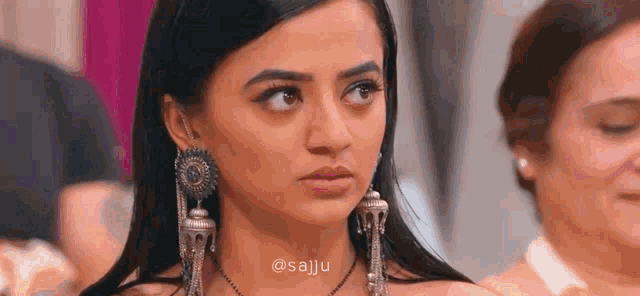 a woman wearing a necklace and earrings is looking at the camera .