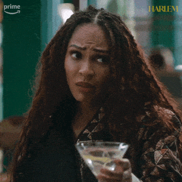 a woman with dreadlocks is holding a martini in front of a sign that says prime