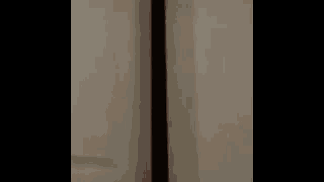 a person is standing in front of a white wall with a brown pole .