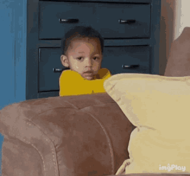a little boy is sitting on a couch with a pillow and looking at the camera .