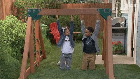 a boy and a girl are playing on a swing set with their arms up