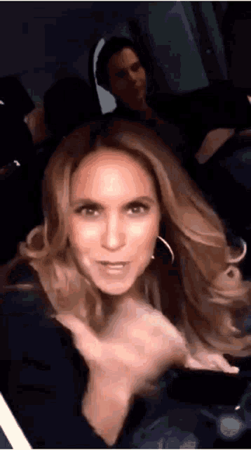 a woman with blonde hair and hoop earrings is sitting in a dark room with a man behind her .
