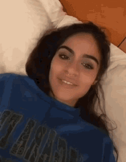 a young woman is laying on a bed wearing a blue sweatshirt .