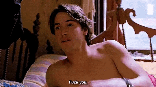 a shirtless man is laying on a bed talking to another man .