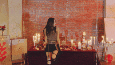 a woman stands in front of a table with candles and a brick wall behind her
